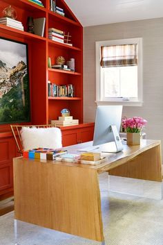 a desk with a laptop on top of it in front of a red bookcase