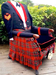 a man in a kilt sitting on top of a wooden bench next to bushes