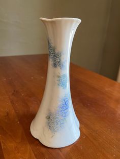 a white vase with blue flowers on it sitting on a wooden table next to a wall