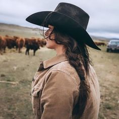 a woman wearing a cowboy hat and standing in front of cows on the grass field