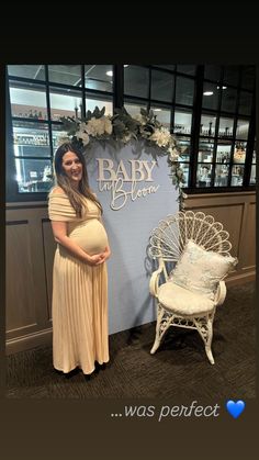 a pregnant woman standing in front of a baby shower sign