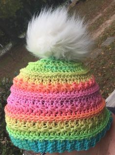 a person wearing a multicolored crocheted hat with a white pom - pom