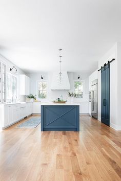 an open kitchen with white cabinets and blue island in the center, hardwood flooring