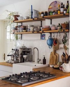 a stove top oven sitting inside of a kitchen next to a wooden shelf filled with pots and pans