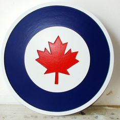 a blue and white plate with a red maple leaf painted on the front, against a white wall