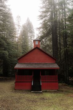 a small red building in the middle of a forest filled with tall trees and grass