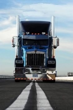 a blue semi truck driving down a road under a blue sky with puffy clouds