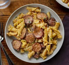 a plate of pasta with sausage and potatoes on it next to silverware, fork and napkin