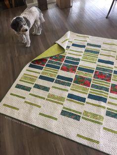 a dog standing on the floor next to a quilted table runner that has been made