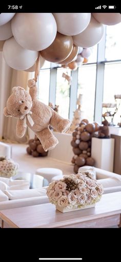 a teddy bear hanging from a bunch of balloons in a room with other items on the table