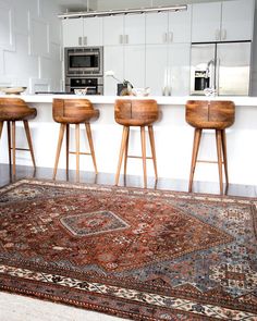 three wooden stools sitting on top of a rug in front of a kitchen counter