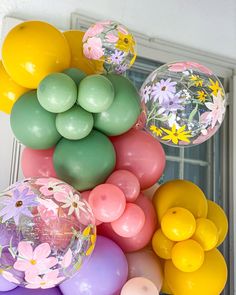 a bunch of balloons that are on top of each other in front of a window