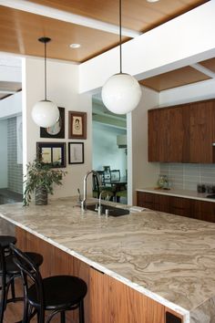 a large kitchen with marble counter tops and wooden cabinets, along with black bar stools