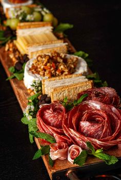 an assortment of meats and cheeses are arranged on a long wooden platter