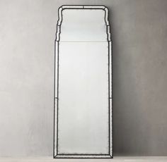 a tall mirror sitting on top of a wooden floor next to a white wall mounted shelf