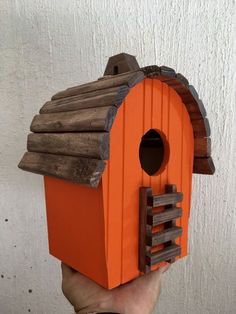 a hand holding up a small birdhouse made out of wood and orange paint on the outside