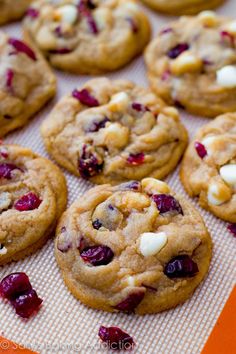 cookies with cranberries and white chocolate chips are on a baking sheet, ready to be eaten