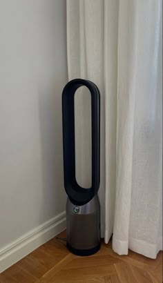 an air purifier sitting on the floor next to a window with white curtains