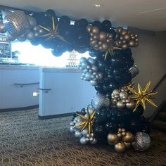 a balloon arch decorated with black and silver balloons, gold starbursts and other decorations