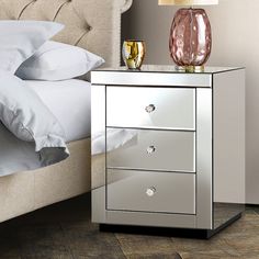 a mirrored bedside table with two drawers and a pink vase on the nightstand next to it