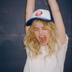 a woman with her hands up in the air while wearing a baseball cap and screaming