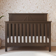 a baby crib in front of a wall with leaves on it and a potted plant next to it