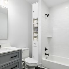 a white toilet sitting next to a bath tub under a bathroom mirror with lights on