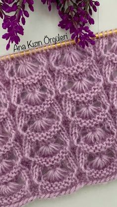 a close up of a knitted object with purple flowers in the background