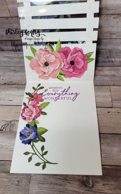 a white card with pink and blue flowers on it, sitting on top of a wooden table