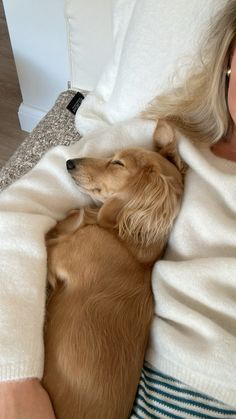 a woman laying in bed next to a brown dog sleeping on top of her stomach