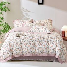 a bed with pink and white comforters in a room next to a potted plant