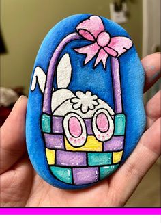 a hand holding a painted rock with an image of a bunny in a basket on it