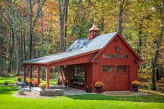 a red barn in the woods with lots of trees and flowers on the grass around it