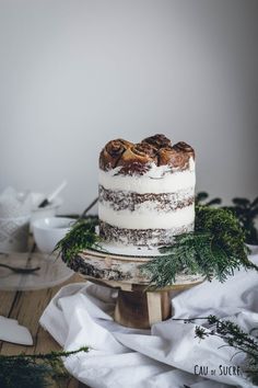 a cake sitting on top of a wooden table covered in frosting and greenery