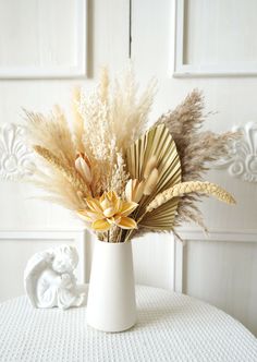 a white vase filled with dried flowers on top of a table