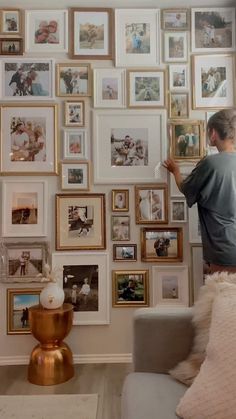 a woman standing in front of a wall full of pictures and framed photos on it