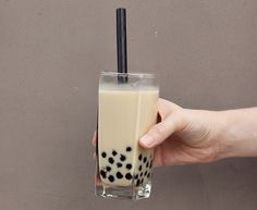 a hand holding a drink with black dots on the top and a straw sticking out of it