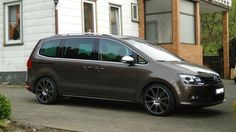 a brown van parked in front of a white house with black wheels and rims