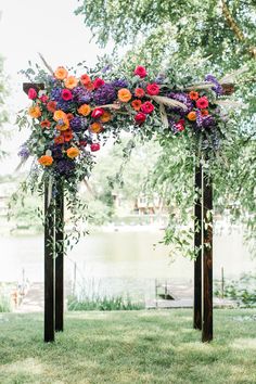 an outdoor wedding ceremony with flowers and greenery on the arch over the water's edge