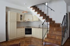 a kitchen with white cabinets and brown tile flooring next to a staircase leading up to the second floor