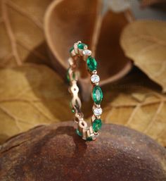 an emerald and diamond ring sitting on top of a rock