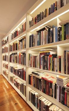 a bookshelf filled with lots of books on top of wooden flooring next to a white wall