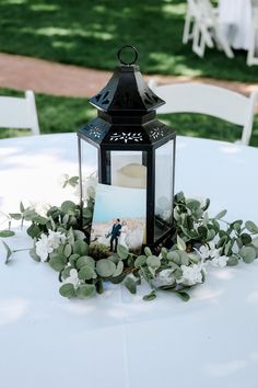 a lantern is sitting on top of a table with flowers and greenery around it