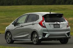 the rear end of a silver honda fit hatchback on a road with grass in the background