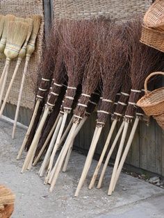 brooms lined up on the side of a building with wicker baskets hanging from them