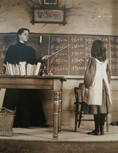 an old black and white photo of two children in front of a chalkboard with writing on it