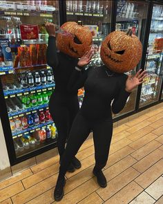 two women in black outfits holding up pumpkin heads