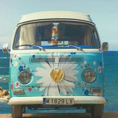 an old vw bus with flowers painted on the front parked by the water's edge