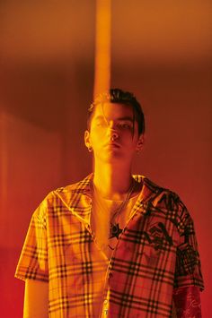 a man wearing glasses and a plaid shirt standing in front of a red wall with his eyes closed