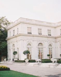 a large white building with two horses in the front yard and bushes on either side